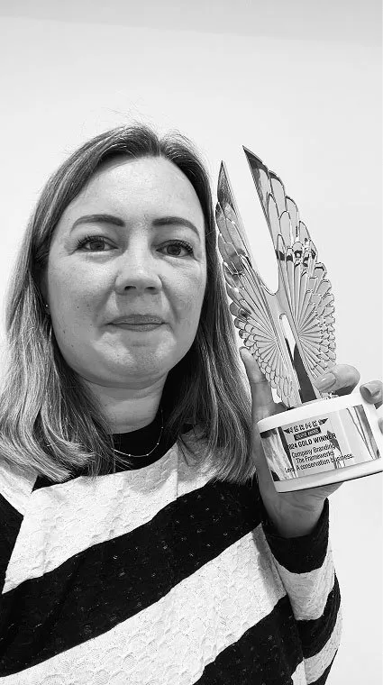 A woman holding up a winged Hermes Creative Awards trophy in a black-and-white photo.