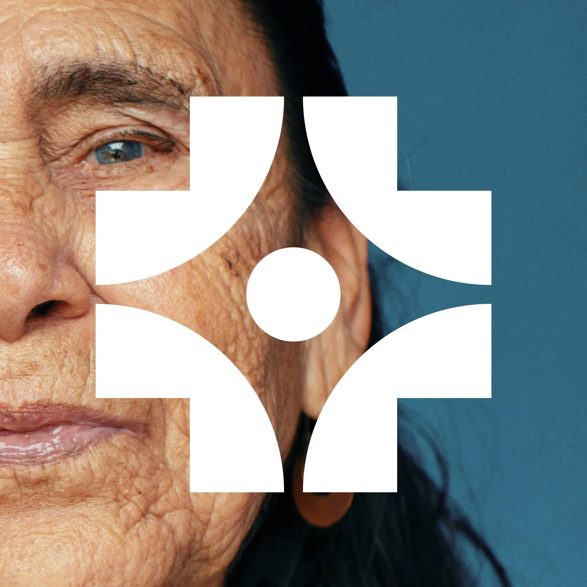 Close-up portrait of an older woman with blue eyes against a blue background, overlaid with a large white geometric logo of a central circle surrounded by four curved brackets.